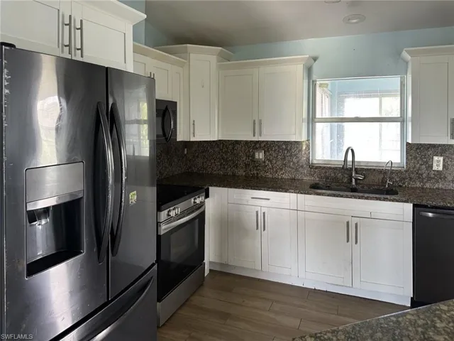 Kitchen featuring white cabinetry with silver hardware, dark patterned countertops and matching backsplash, a stainless-steel range, and wood-finish flooring