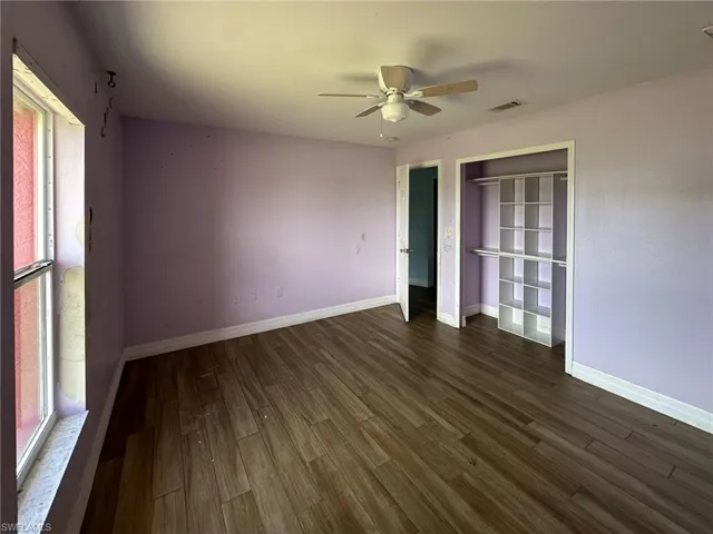 Spacious room featuring wood-finish flooring, a built-in closet organization system, overhead ceiling fan, and a wide window with natural light