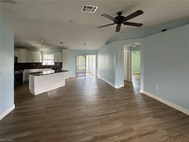 Open concept living area featuring wood-finish tile flooring, a kitchen island with dark countertops, white cabinetry with dark hardware, a built-in oven, and a ceiling fan with integrated lighting