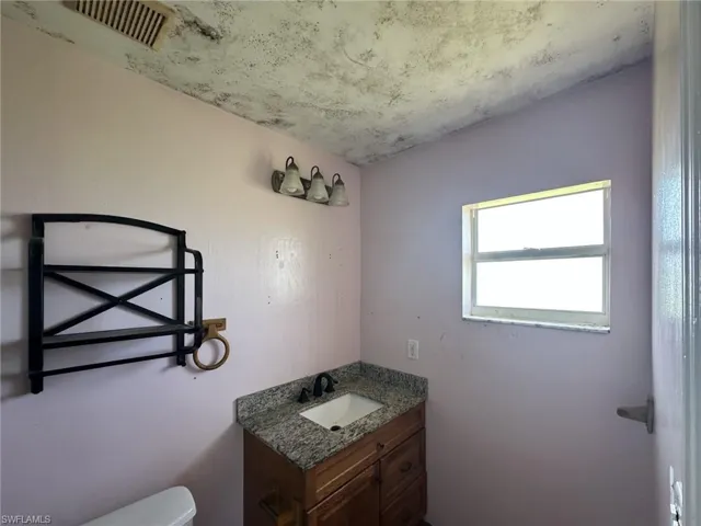 Single-pane window featuring a vanity with a granite countertop, undermount sink, and matte black faucet