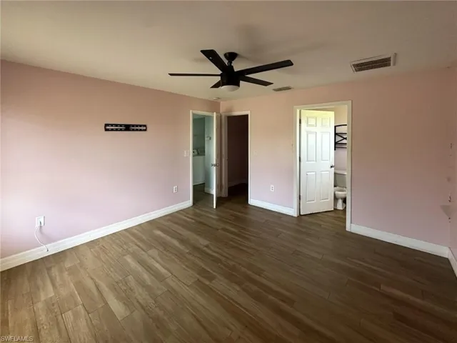 Spacious interior room featuring wood-finish flooring, a ceiling fan, and white baseboards