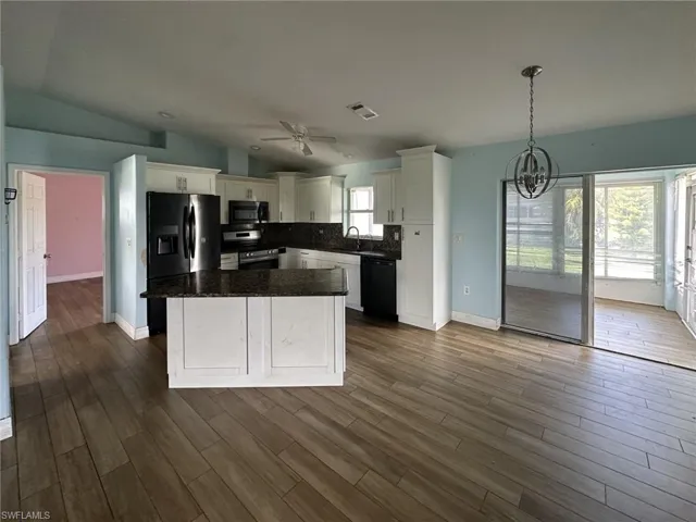 Open-concept kitchen featuring wood-finish flooring, white cabinetry, dark stone countertops, black appliances, and a central island with breakfast bar seating