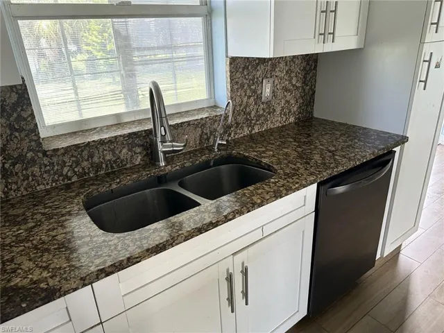 Kitchen counter featuring a double basin sink with a contemporary faucet, granite countertops, and a full-height backsplash