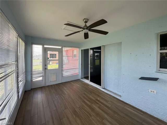 Enclosed patio featuring wood-finish flooring, a ceiling fan with dark wood-tone blades, and light blue textured walls