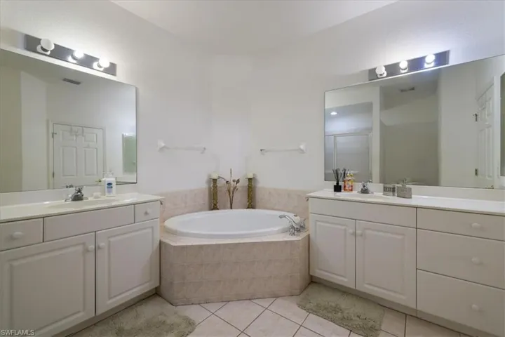 Full bath featuring two vanities, a garden tub, a stall shower, and light tile patterned flooring