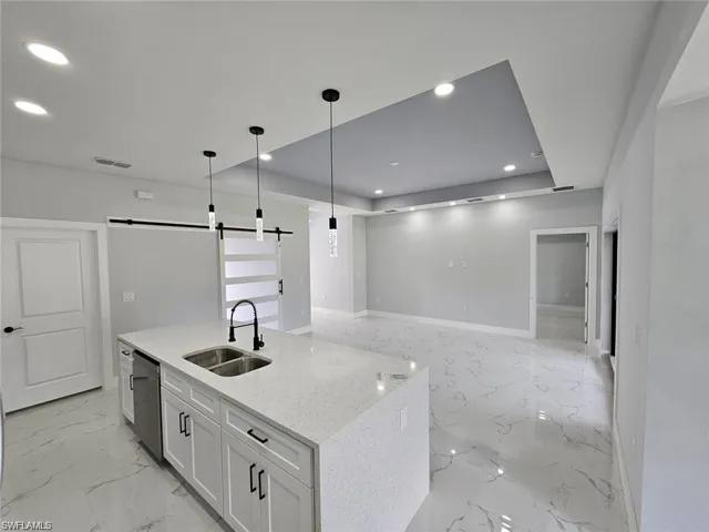 Kitchen featuring sink, a barn door, pendant lighting, stainless steel dishwasher, and white cabinets