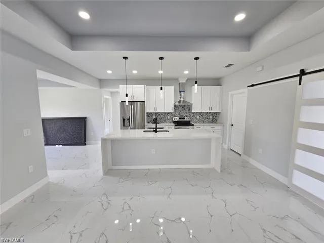 Kitchen featuring wall chimney range hood, white cabinets, appliances with stainless steel finishes, a barn door, and sink