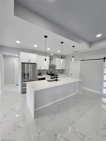 Kitchen with sink, a barn door, pendant lighting, white cabinets, and stainless steel refrigerator with ice dispenser
