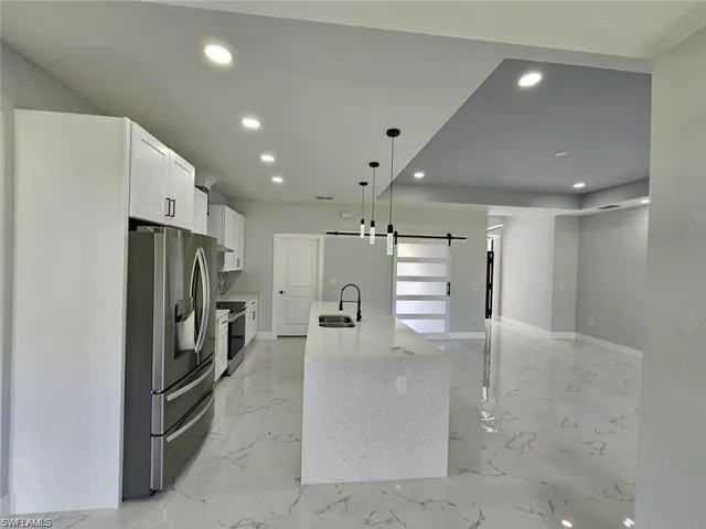 Kitchen featuring an island with sink, light stone countertops, a barn door, white cabinets, and appliances with stainless steel finishes