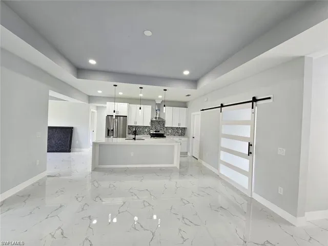 Kitchen featuring a kitchen island with sink, stainless steel appliances, a barn door, decorative light fixtures, and white cabinets