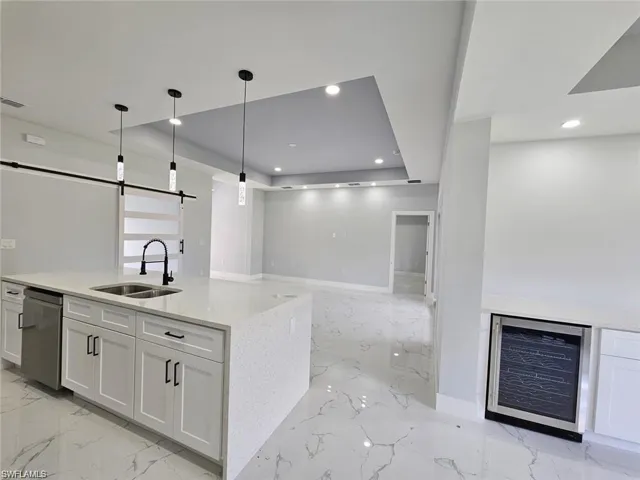 Kitchen featuring light stone counters, white cabinetry, a barn door, dishwasher, and sink