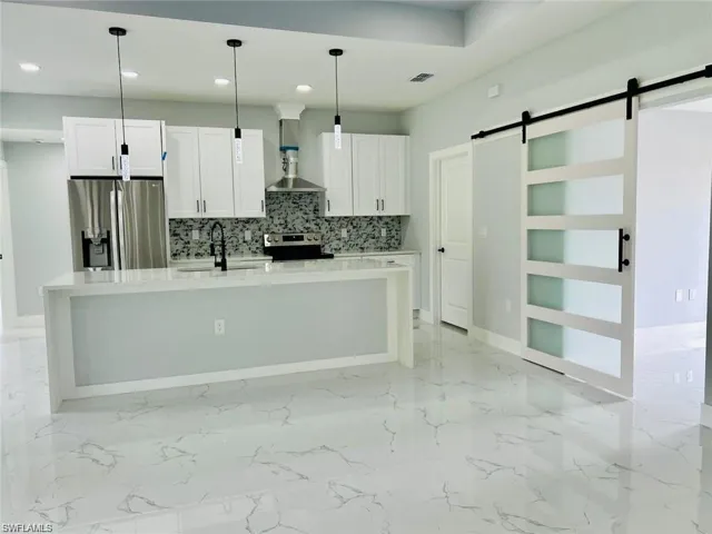 Kitchen with stainless steel appliances, hanging light fixtures, a barn door, and white cabinets