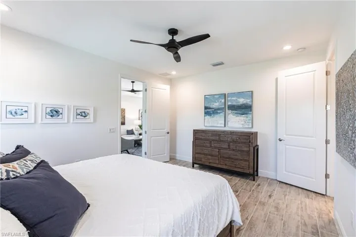 Bedroom with light hardwood / wood-style floors and ceiling fan. All windows are impact resistant.