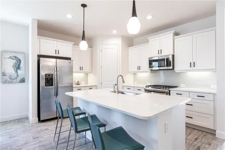 Kitchen featuring white cabinetry, sink, hanging pendant light fixtures, a kitchen island with sink, and stainless steel appliances