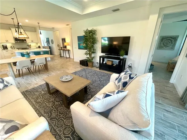 Living area featuring ceramic wood finish floors, visible vents, baseboards, and crown molding