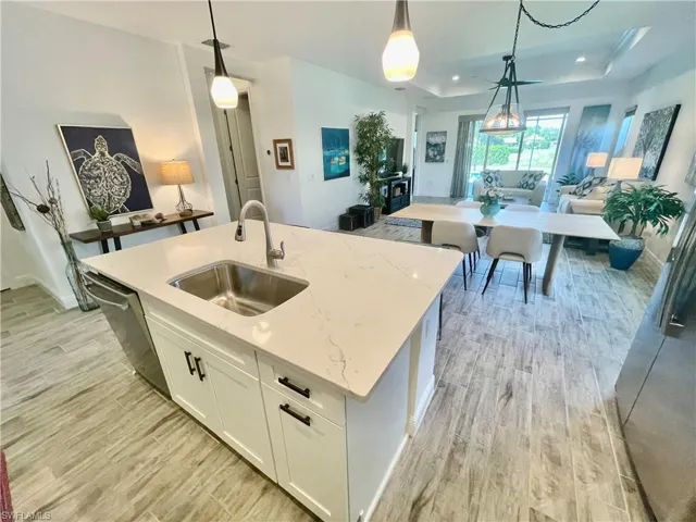 Kitchen with quartz counter tops, with a sink, decorative light fixtures, open floor plan, ceramic wood finished floors, and dishwasher