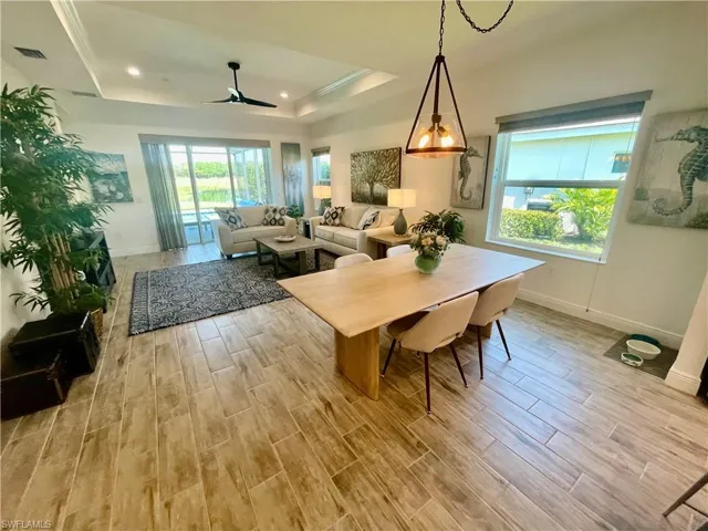 Dining space with a wealth of natural light, visible vents, a raised ceiling, and ceramic wood finish floors and fan in family room.