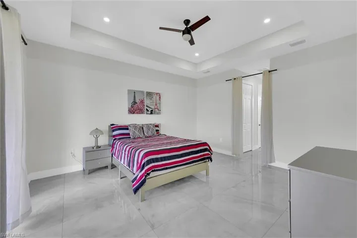 Bedroom featuring baseboards, a raised ceiling, marble finish floor, and recessed lighting