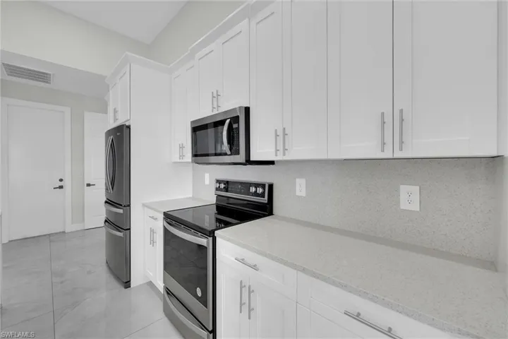 Kitchen featuring tasteful backsplash, white cabinets, visible vents, light stone counters, and stainless steel appliances
