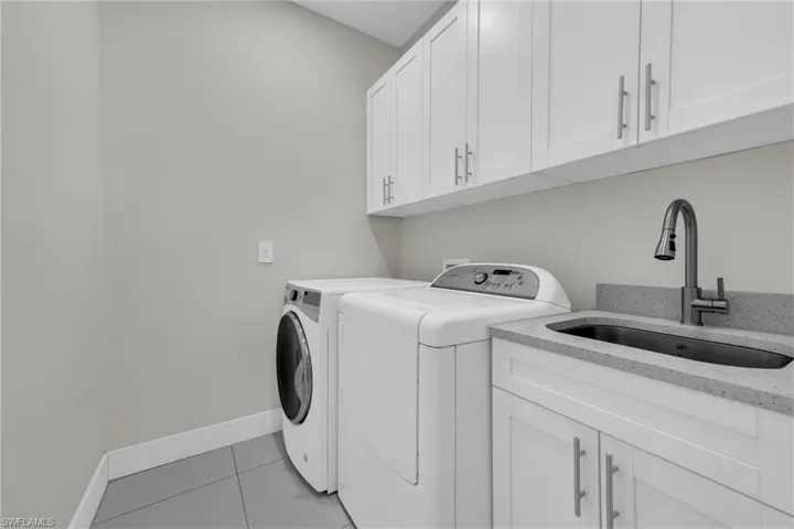 Laundry area featuring baseboards, light tile patterned flooring, washer and clothes dryer, cabinet space, and a sink