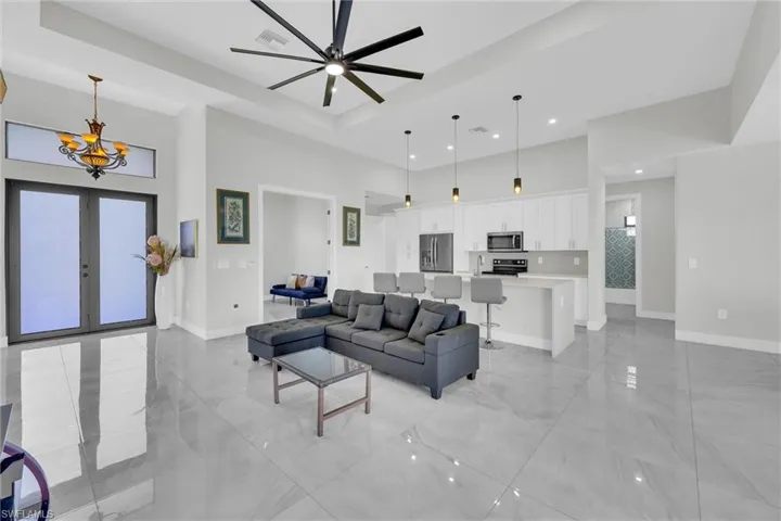 Living area featuring visible vents, baseboards, a high ceiling, ceiling fan with notable chandelier, and marble finish floor
