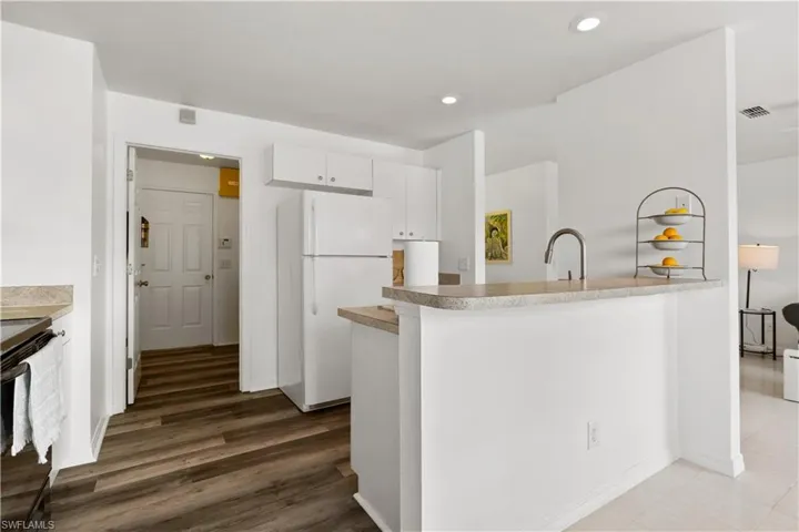 Kitchen with black / electric stove, white cabinets, kitchen peninsula, dark hardwood / wood-style flooring, and white fridge