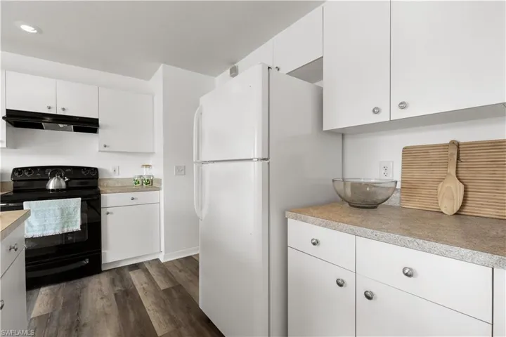 Kitchen with white cabinets, white refrigerator, black range with electric stovetop, and dark hardwood / wood-style flooring