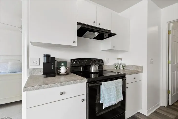 Kitchen featuring hardwood / wood-style flooring, black electric range, and white cabinetry