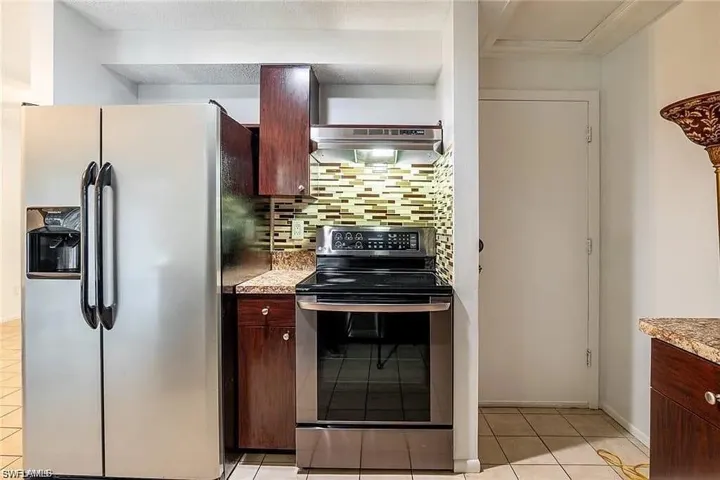 Kitchen with appliances with stainless steel finishes, tasteful backsplash, light tile patterned floors, under cabinet range hood, and light countertops