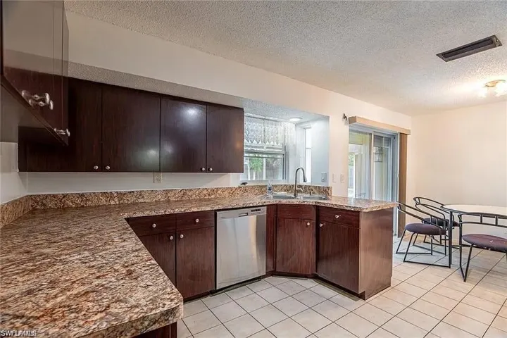 Kitchen with a textured ceiling, dishwasher, dark brown cabinetry, light tile patterned floors, and a peninsula