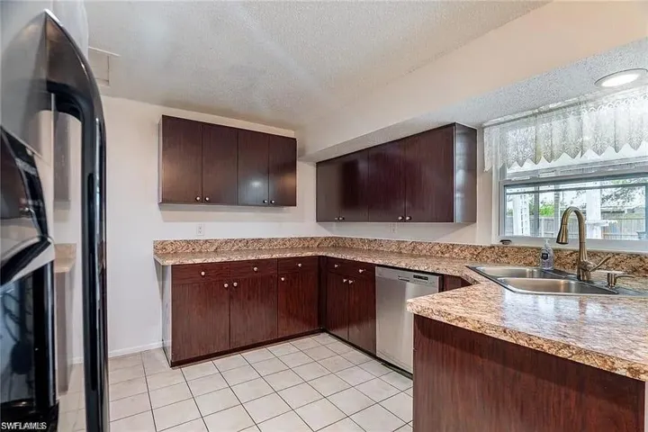 Kitchen with black refrigerator, a textured ceiling, dishwasher, light countertops, and dark brown cabinets