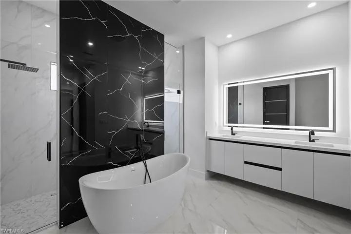 Bathroom with marble tiled flooring, double vanity, a freestanding bath, a marble finish shower, and recessed lighting