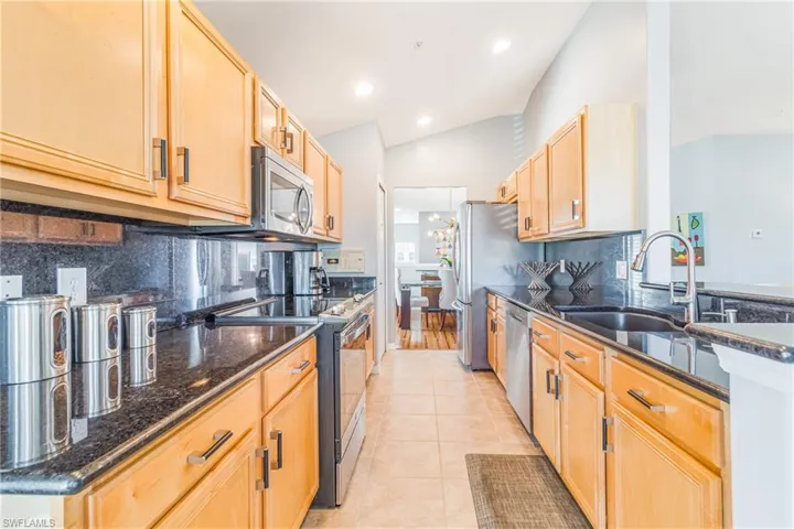 Kitchen with light cabinetry, granite backsplash & countertops, stainless steel appliances,  and vaulted ceiling