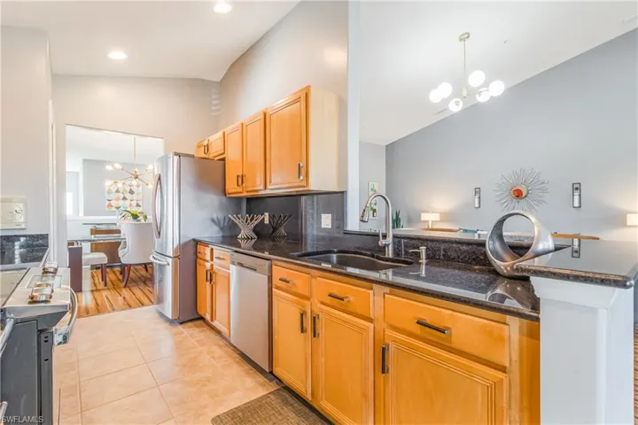 Kitchen vaulted ceiling, stainless steel appliances, granite counters, and light cabinets