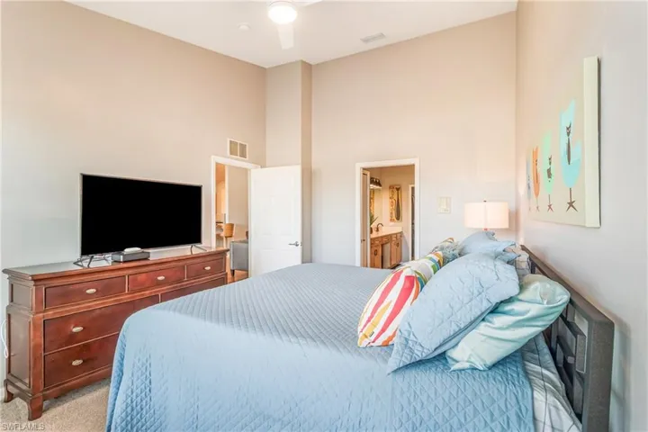 Bedroom featuring light carpet, ensuite bathroom, ceiling fan, and a vaulted ceiling