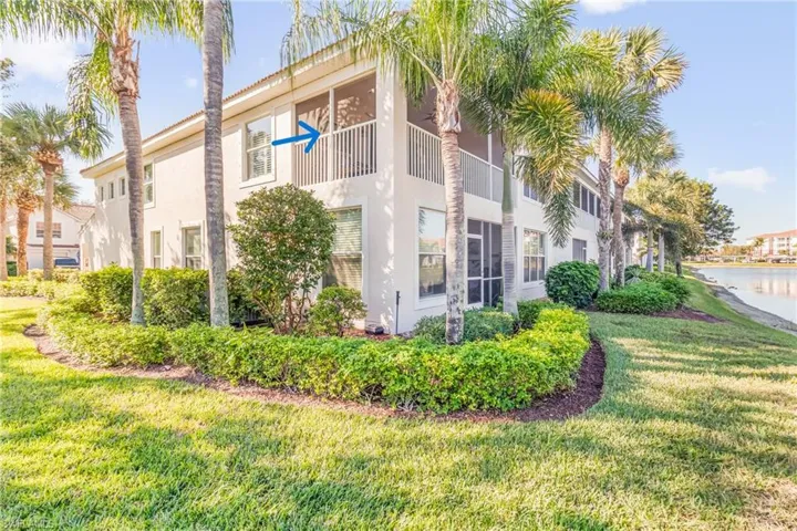View of side of property featuring a balcony, stucco siding, a lawn, and a water view