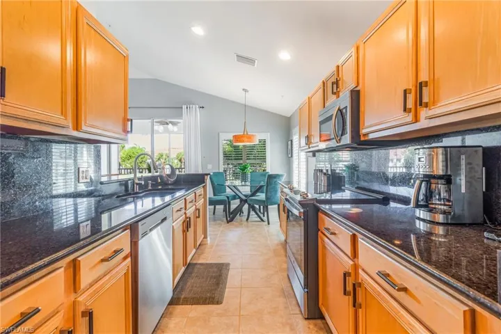 Kitchen with backsplash, stainless steel appliances, dark stone countertops, light tile patterned floors, and vaulted ceiling