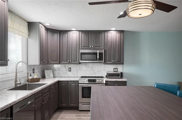 Kitchen with light wood-type flooring, stainless steel appliances, backsplash, a sink, and a ceiling fan