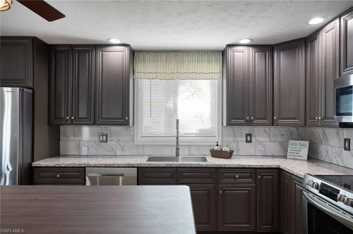 Kitchen with ceiling fan, a sink, backsplash, and appliances with stainless steel finishes