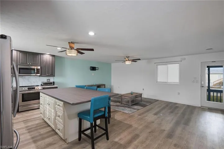 Kitchen featuring decorative backsplash, stainless steel appliances, a ceiling fan, open floor plan, and a breakfast bar area