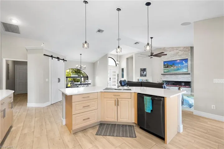 Kitchen featuring a barn door, black dishwasher, open floor plan, light countertops, and light brown cabinetry