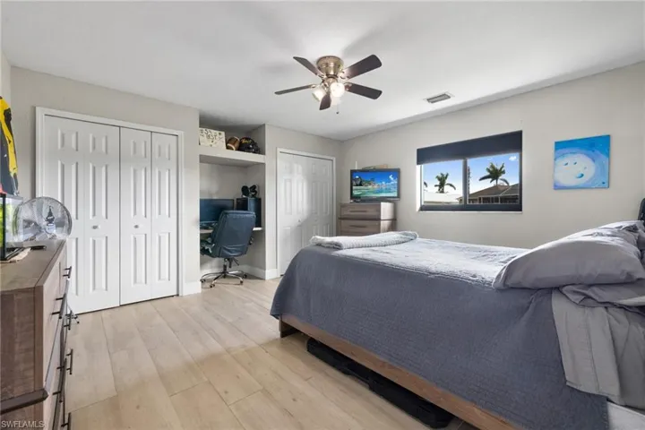 Bedroom with ceiling fan, visible vents, baseboards, light wood-type flooring, and two closets