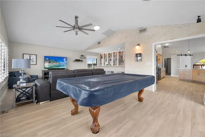 Recreation room featuring ceiling fan, brick wall, visible vents, vaulted ceiling, and light wood finished floors