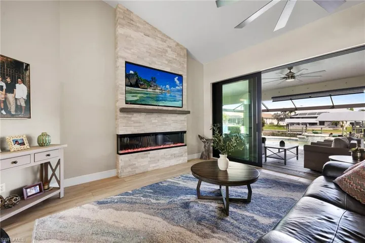 Living room featuring ceiling fan, a stone fireplace, wood finished floors, high vaulted ceiling, and baseboards