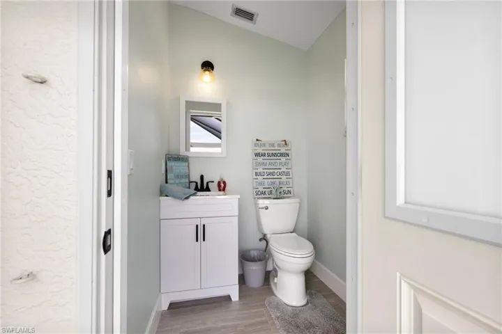 Bathroom featuring visible vents, toilet, vanity, wood finished floors, and baseboards