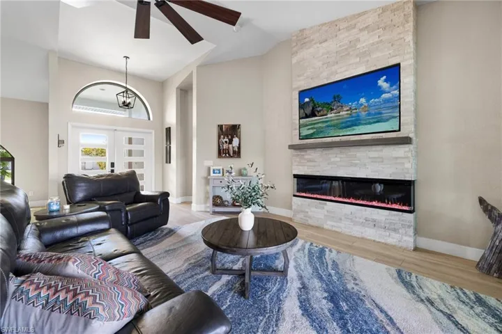 Living room with baseboards, wood finished floors, a stone fireplace, a high ceiling, and french doors
