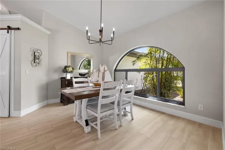 Dining room with light wood finished floors, a barn door, baseboards, and a notable chandelier