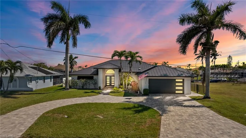Mid-century modern home featuring metal roof, decorative driveway, stucco siding, a standing seam roof, and a front yard