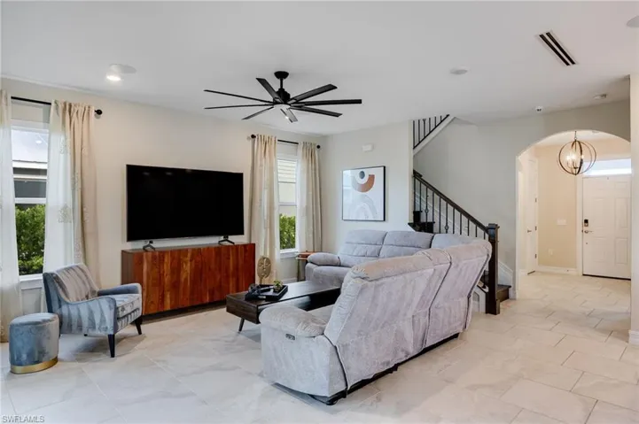Living room featuring stairway, arched walkways, a ceiling fan, and a chandelier