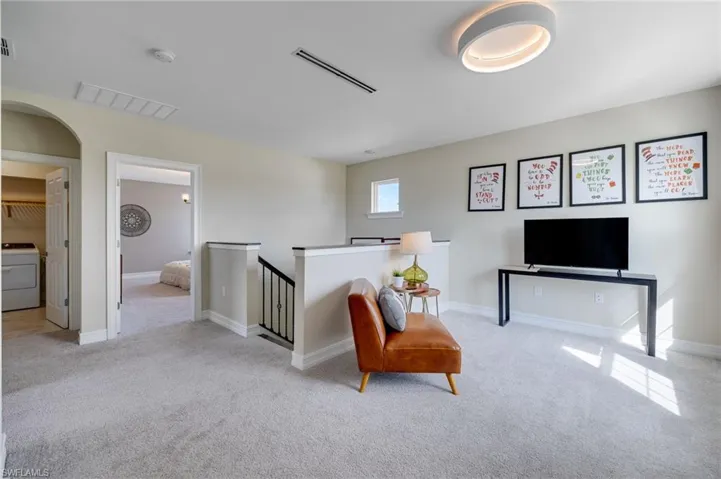 Sitting room with carpet floors, an upstairs landing, washer / dryer, and arched walkways